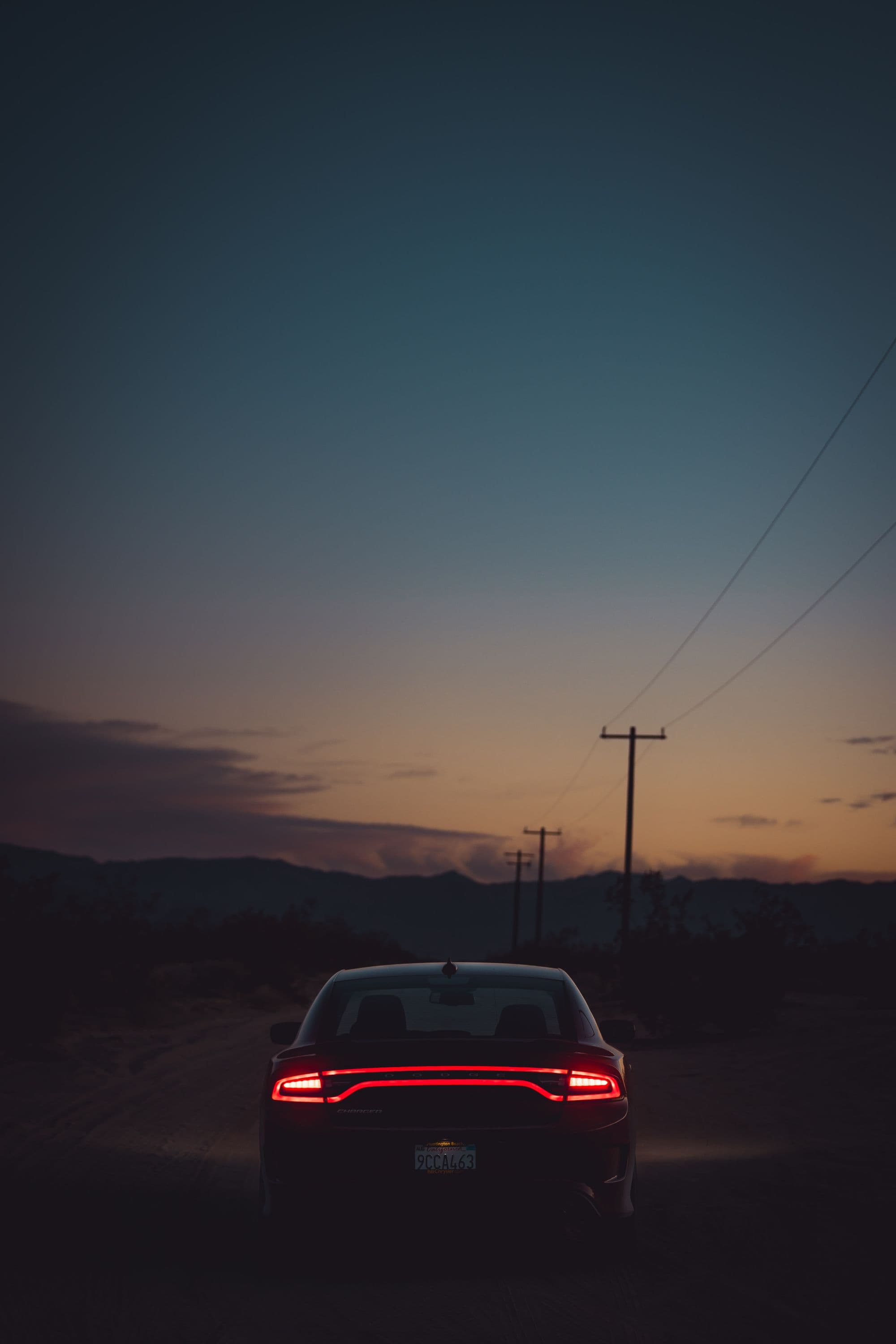 A Dodge Charger from behind on a desert road at dusk, taillight bar glowing